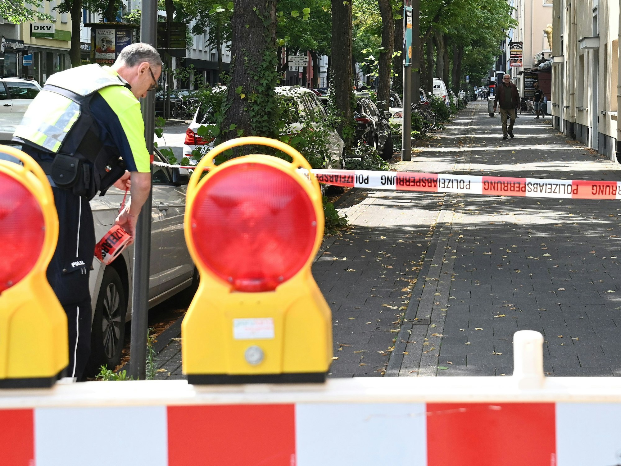 Ein Polizist sperrt einen Fußweg mit Flatterband ab.