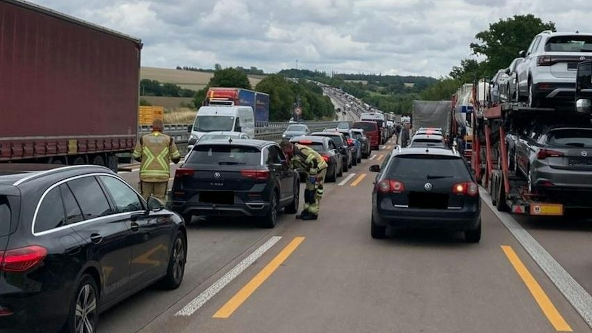 Einsatzkräfte der Feuerwehr gehen von Auto zu Auto, um auf die Rettungsgasse hinzuweisen.