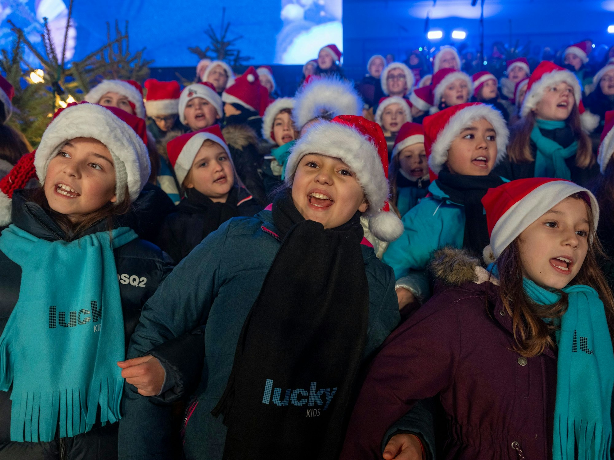 Kinder, die Weihnachtsmann-Mützen tragen, singen lauthals.