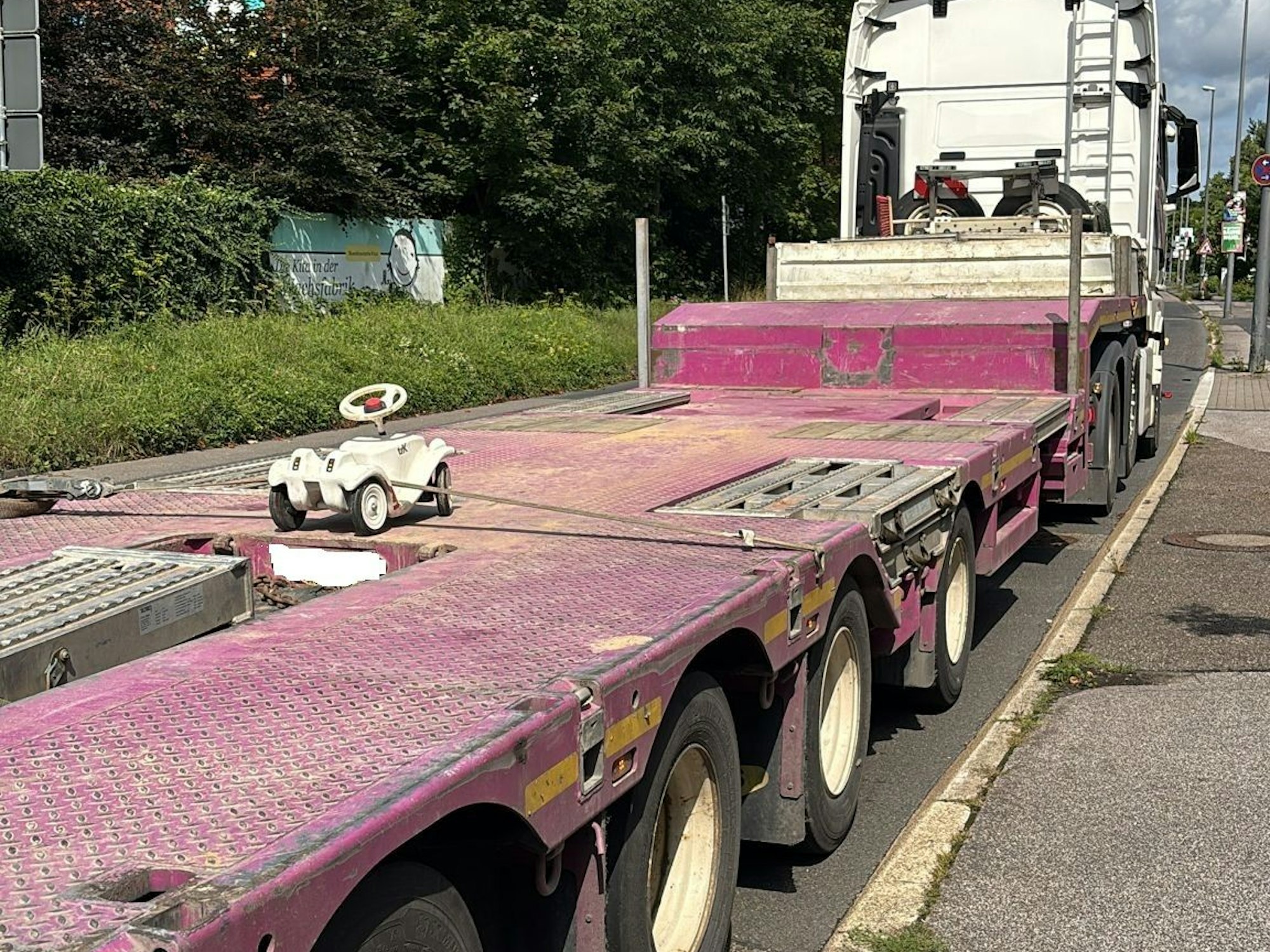 Auf der großen Ladefläche eines Lkw ist ein Bobbycar festgeschnallt.