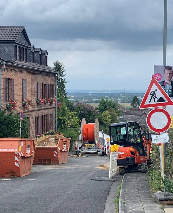 Eine Baustelle mit Absperrungen, Baggern und Schuttcontainern an einer Straße am Hang.