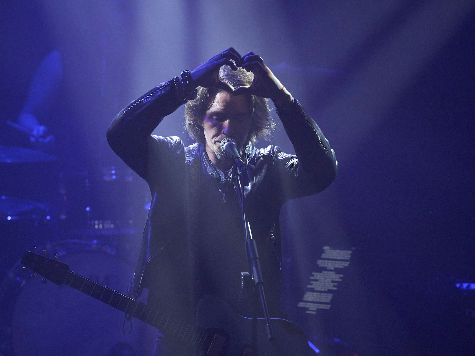 Ein Mann steht hinter einem Mikrofon und bildet mit beiden Händen ein Herz.