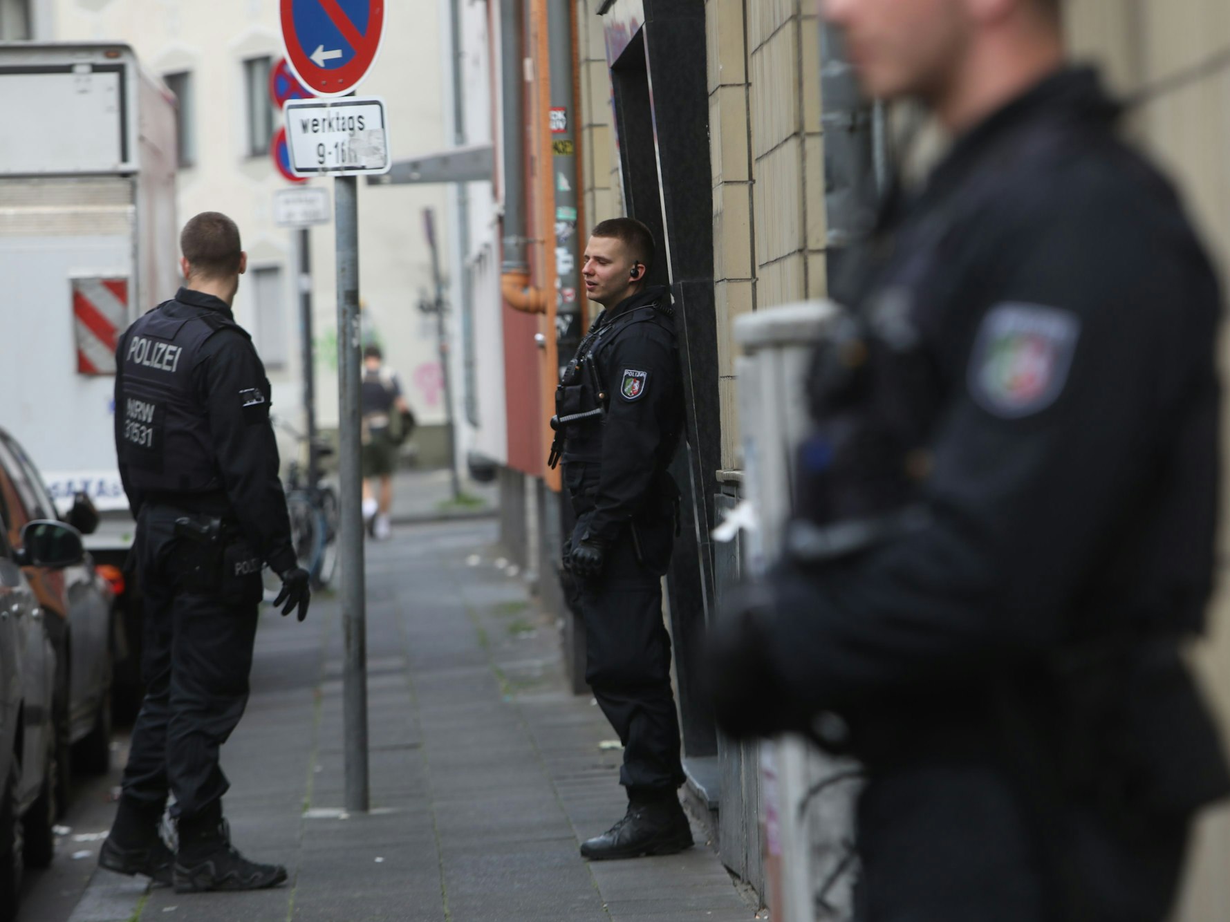 Drei Polizisten stehen vor einer Häuserreihe.