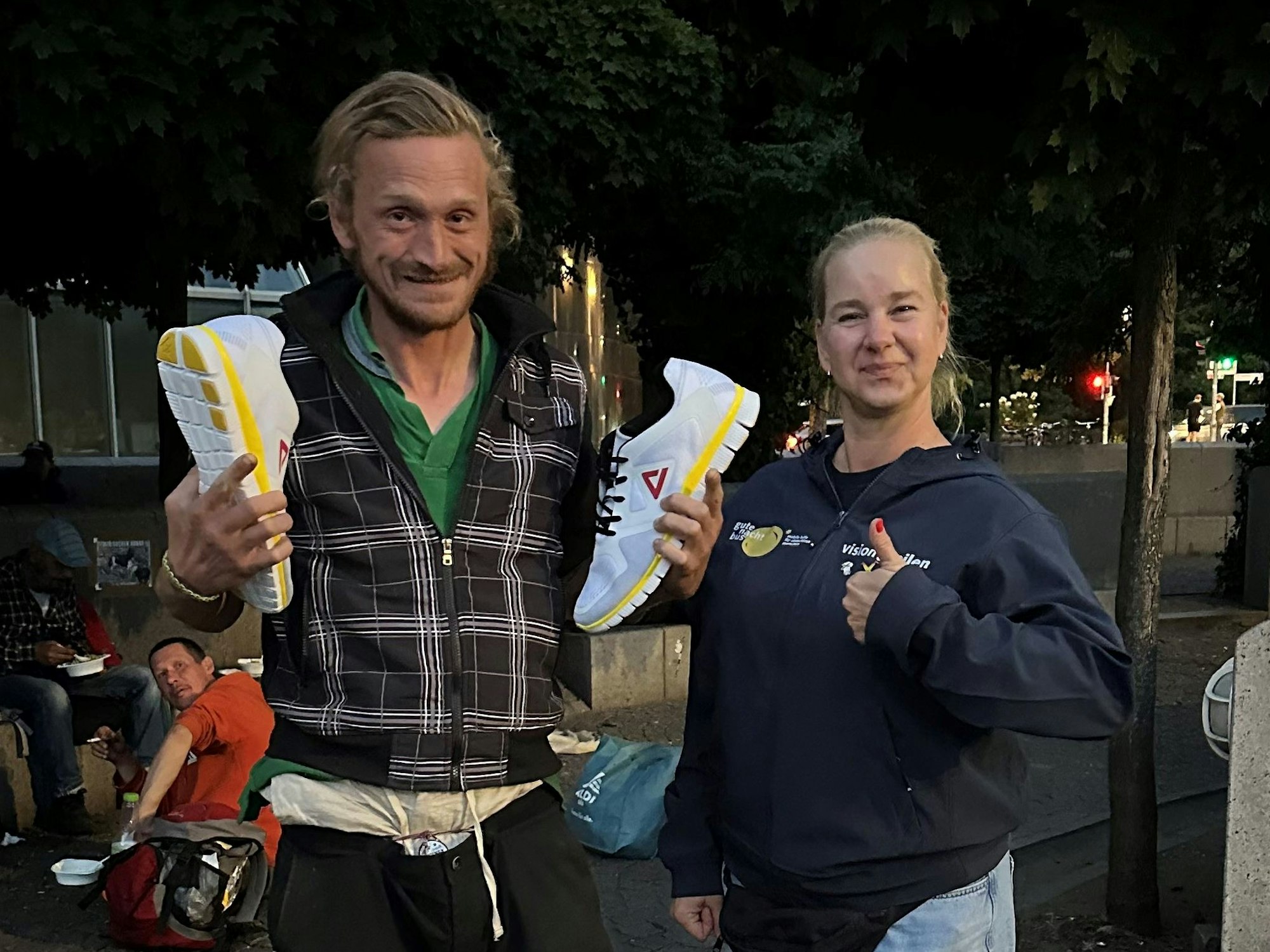 Ein Mann hält Sneaker in den Händen und grinst, neben ihm steht eine Frau.