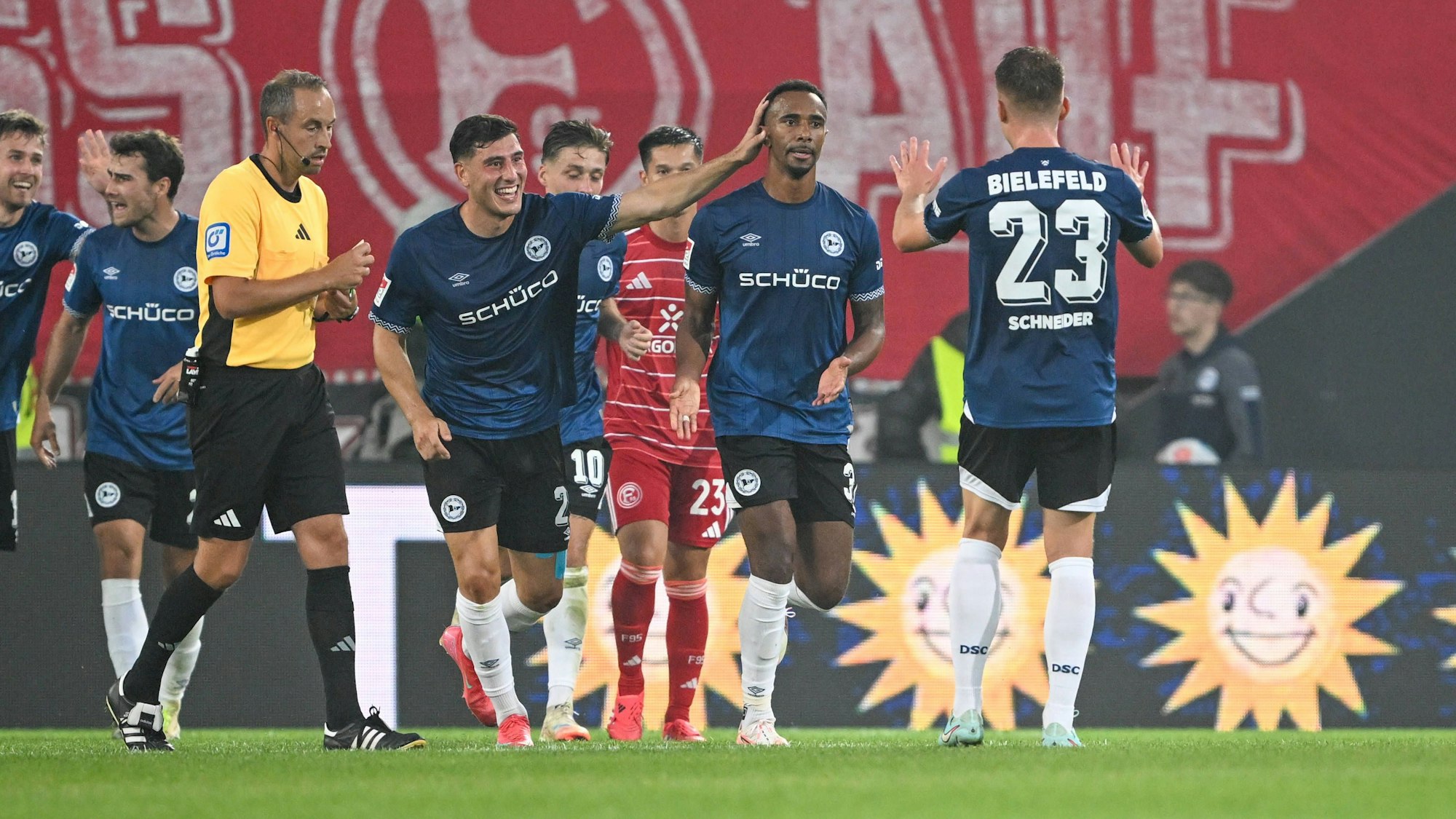 Die Spieler von Arminia Bielefeld jubeln über ein Tor, Schiedsrichter Patrick Alt steht daneben.