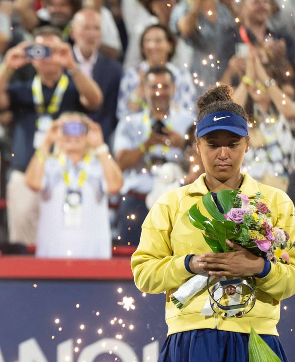 Viktoria Mboko reckt ihre Trophäe in die Höhe, daneben steht die enttäuschte Naomi Osaka.