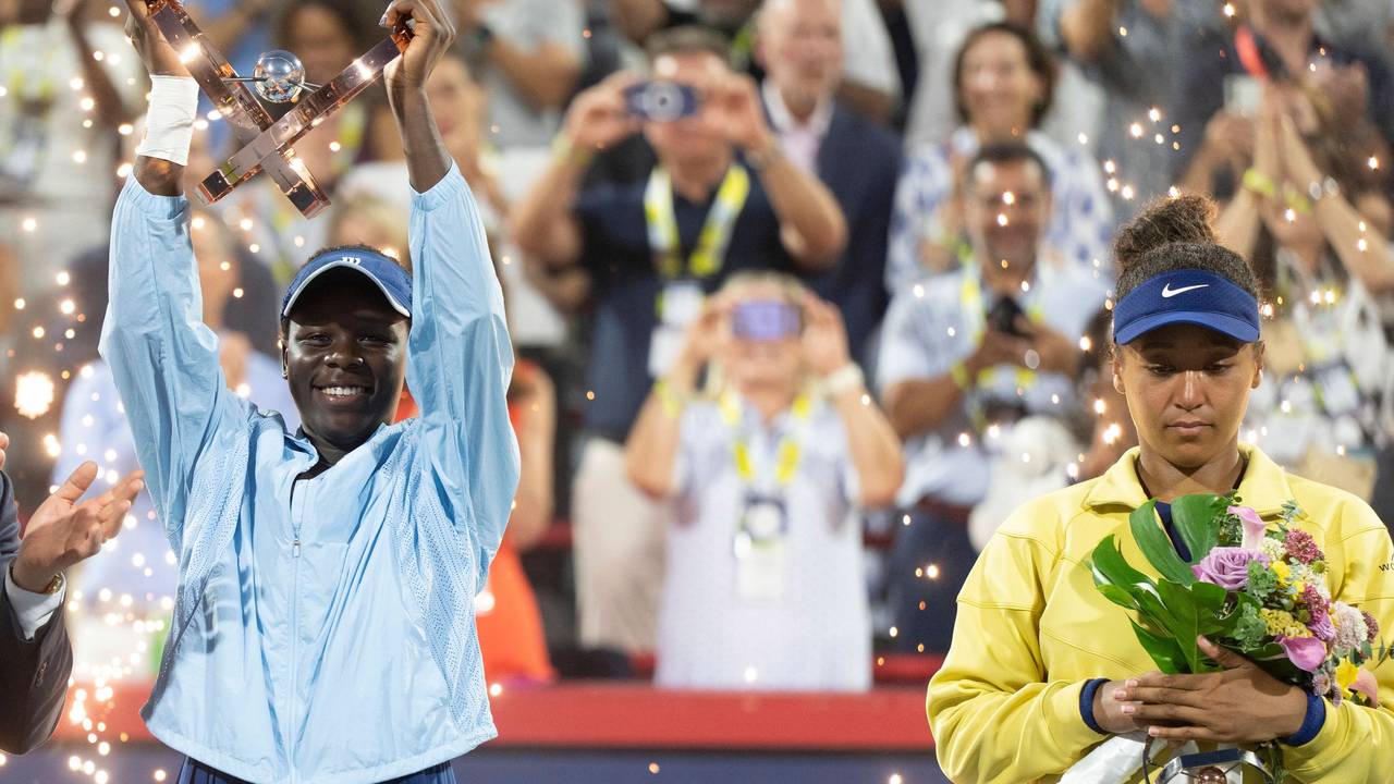 Viktoria Mboko reckt ihre Trophäe in die Höhe, daneben steht die enttäuschte Naomi Osaka.
