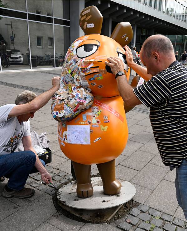 Zwei Mitarbeiter des Westdeutschen Rundfunks (WDR) schieben die etwa 75 Kg schwere Fiberglasskulptur der WDR-Maus zum Senderhaus. Die orangefarbene Maus-Figur wurde bei einem Brandanschlag beschädigt und wird nun repariert.