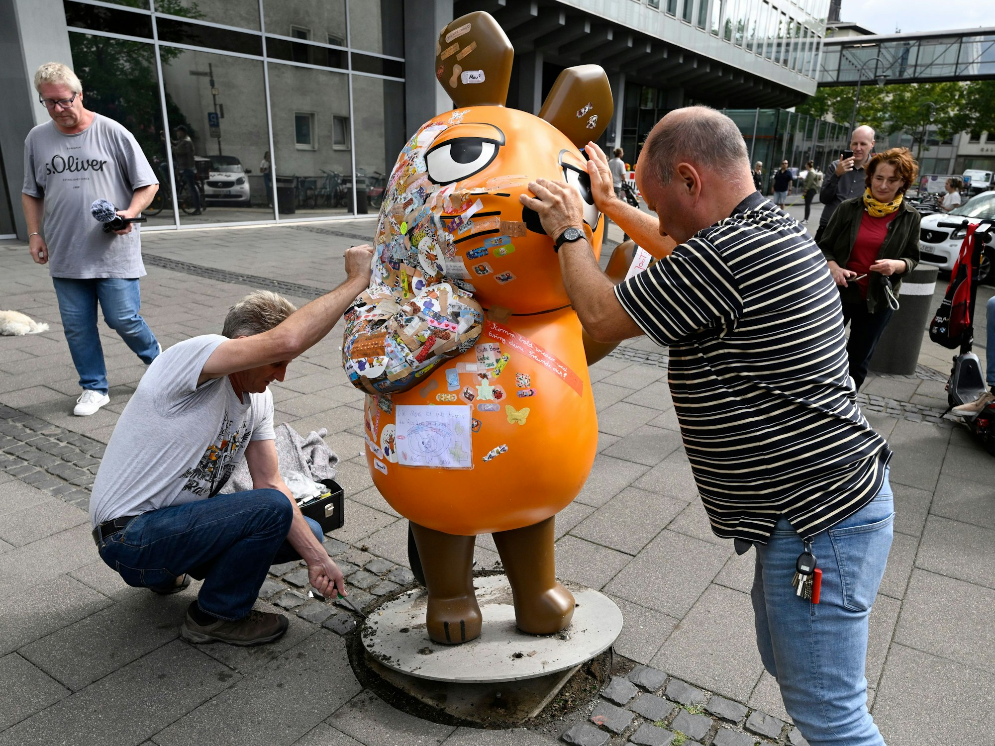 Zwei Mitarbeiter des Westdeutschen Rundfunks (WDR) schieben die etwa 75 Kg schwere Fiberglasskulptur der WDR-Maus zum Senderhaus. Die orangefarbene Maus-Figur wurde bei einem Brandanschlag beschädigt und wird nun repariert.