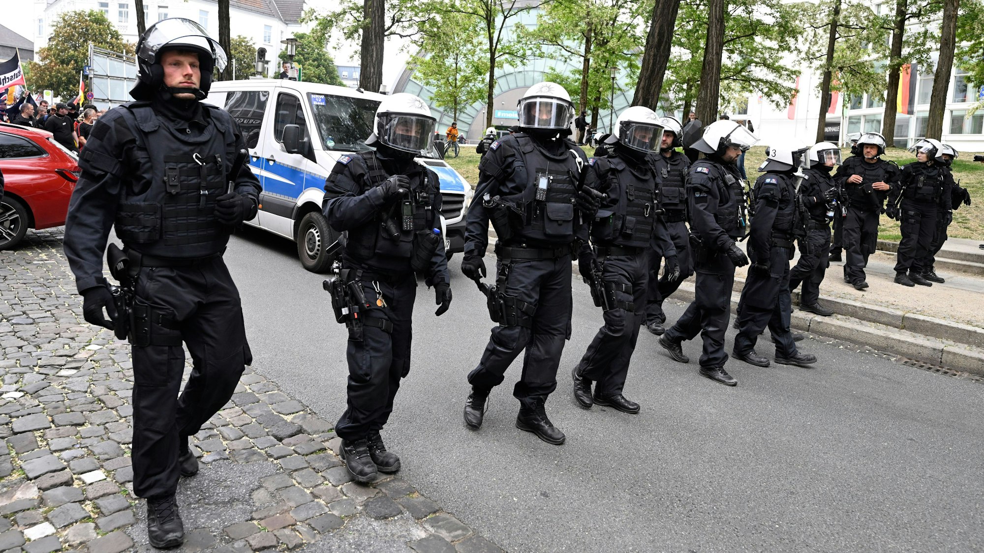 Polizeikräfte, die Helme tragen, gehen nebeneinander eine Straße entlang.