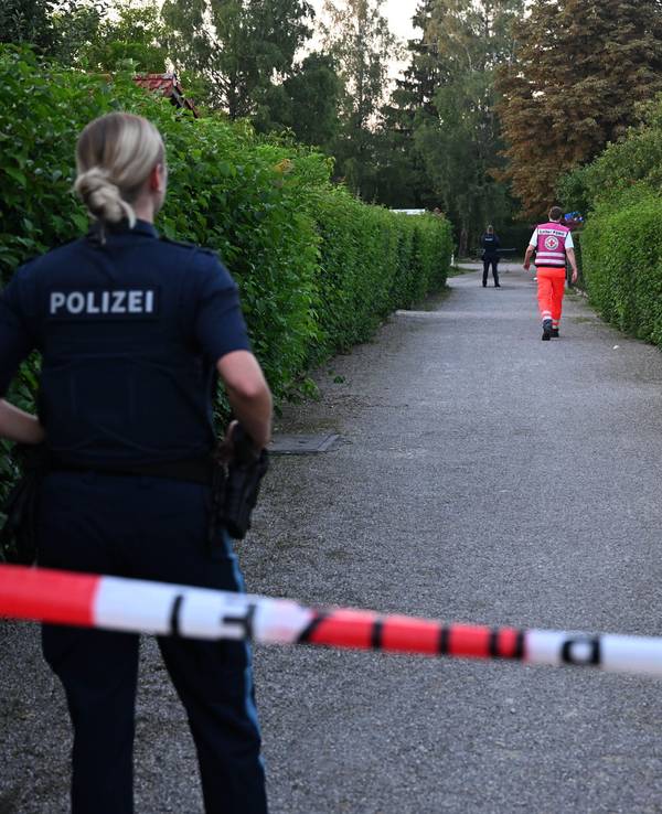 Die Polizei hat einen Gang in einer Kleingartenanlage abgesperrt. Hinter dem Flatterband steht eine Polizistin, weiter entfernt gegen ein Mann vom Rettungsdienst.