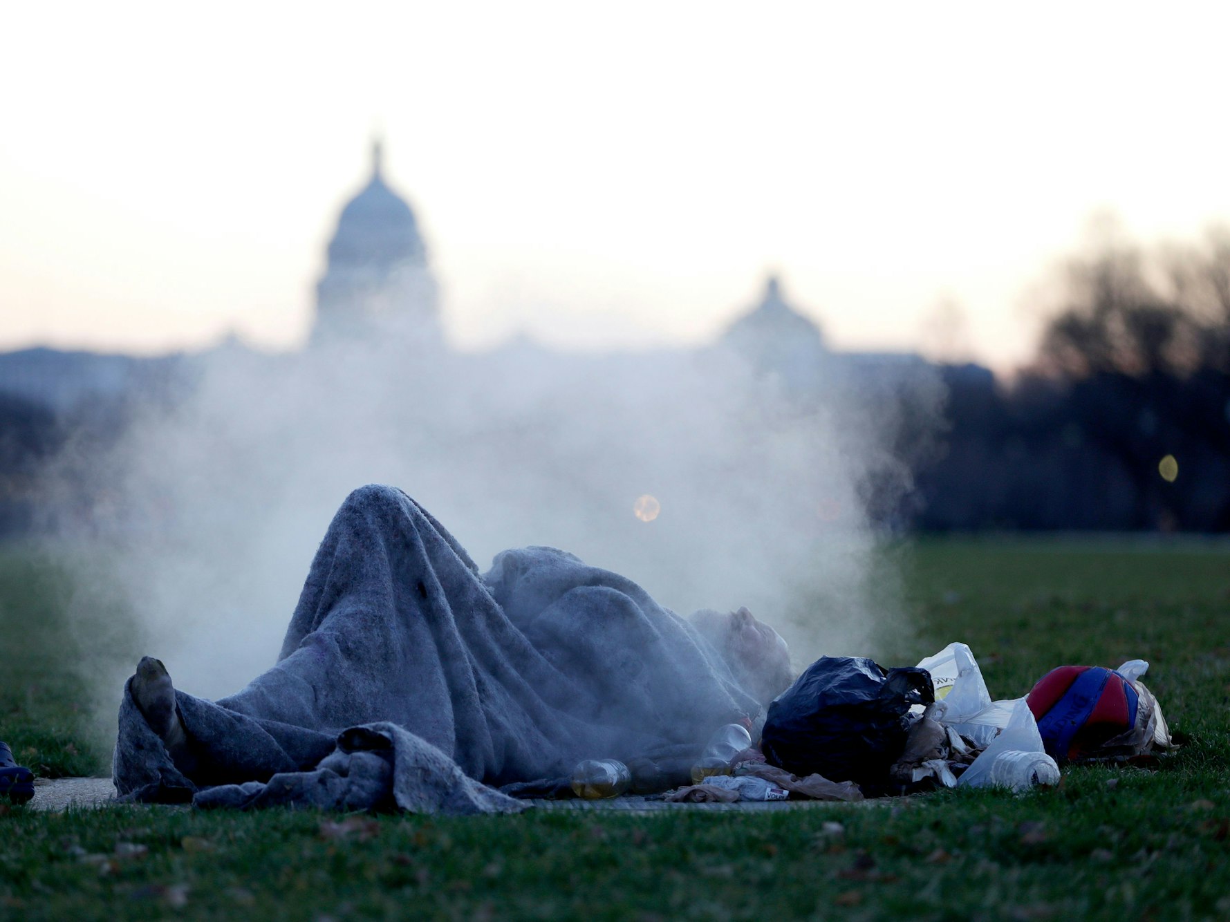 Ein Obdachloser wärmt sich auf einem dampfenden Schacht auf der National Mall auf dem Capitol Hill auf - im Hintergrund ist das US-Kapitol zu sehen. US-Präsident Trump hat Obdachlosen mit der Vertreibung aus der Hauptstadt Washington gedroht.