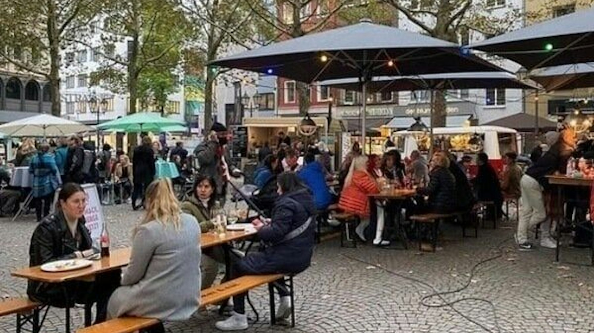 Menschen sitzen unter Schirmen an Tischen und Stühlen, trinken und essen etwas.