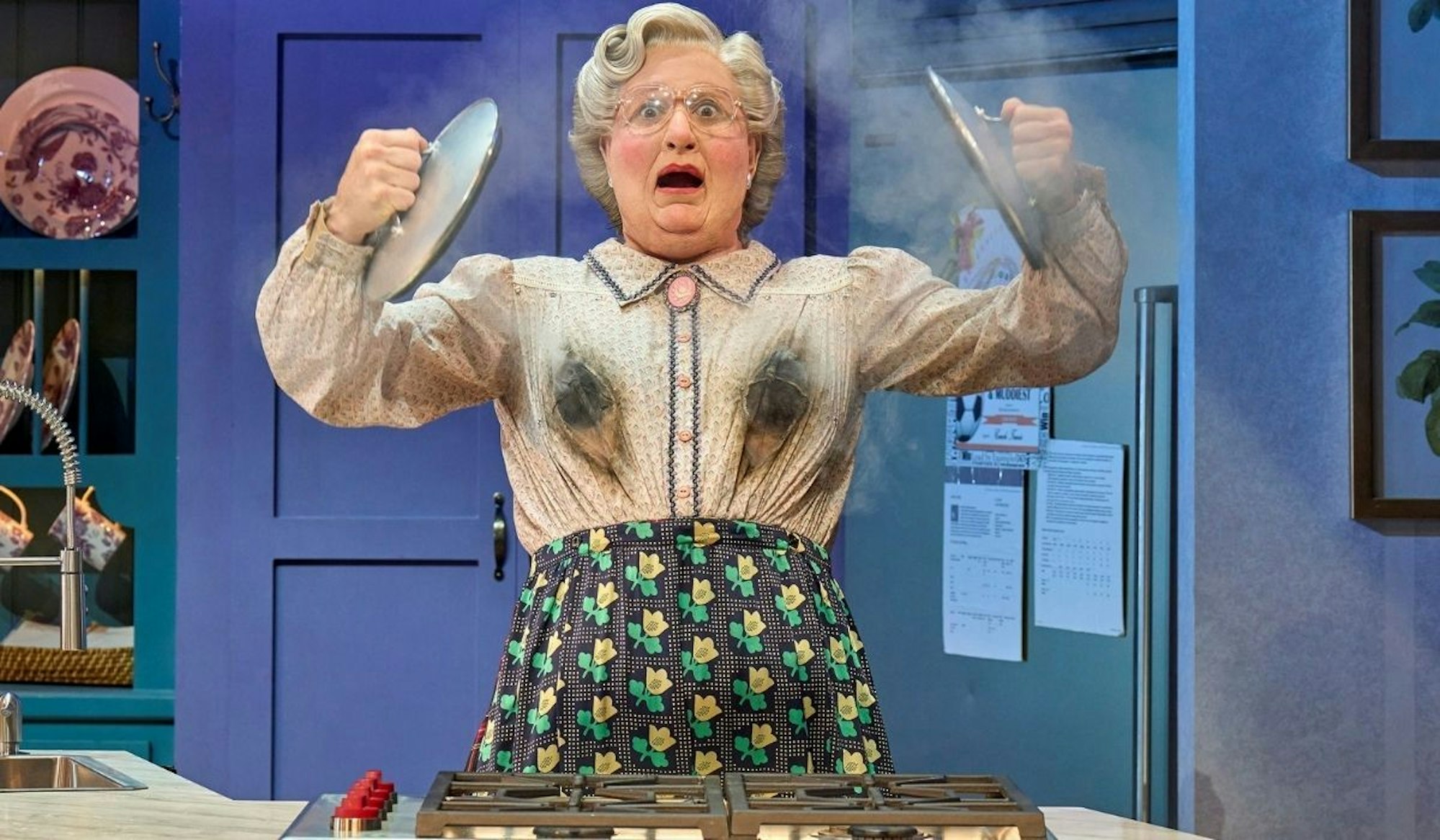 Mrs. Doubtfire sorgt für Chaos in der Küche, indem ihre Bluse beim Kochen Feuer fängt.