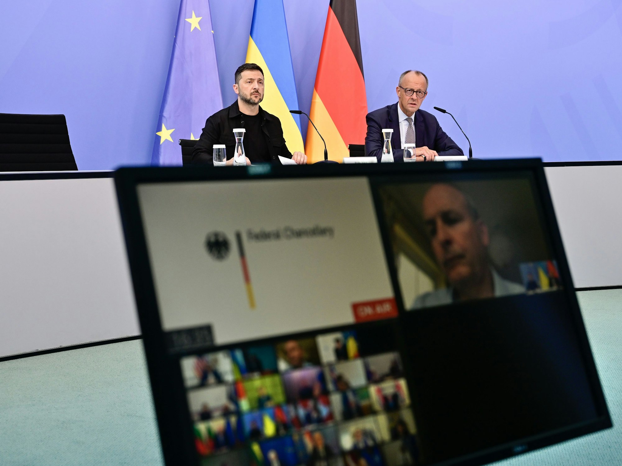 Wolodymyr Selenskyj, Präsident der Ukraine, und der deutsche Bundeskanzler Friedrich Merz sitzen an einem Tisch, davor steht ein Bildschirm.
