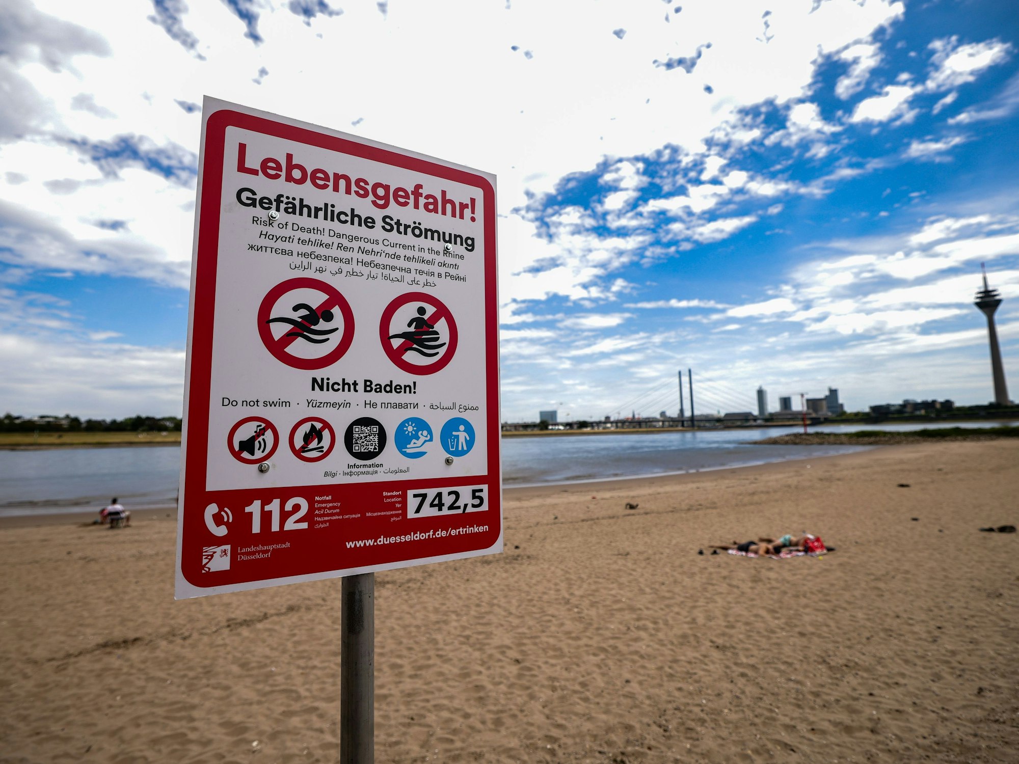 Ein Hinweisschild am Paradiesstand in Düsseldorf weist auf die Gefahren beim Schwimmen im Rhein hin. Ab Donnerstag gilt auch hier das Badeverbot.