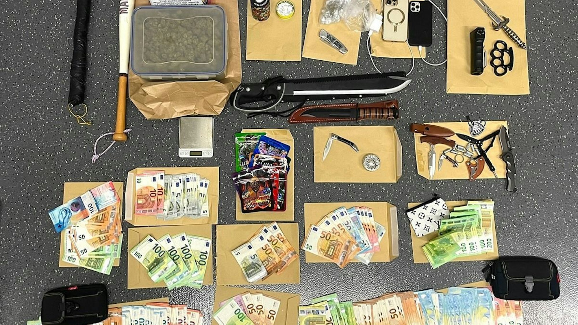 Sichergestellte Gegenstände bei einer Polizeirazzia: Mehrere Waffen, Drogen und Bargeld liegen auf einem Tisch.