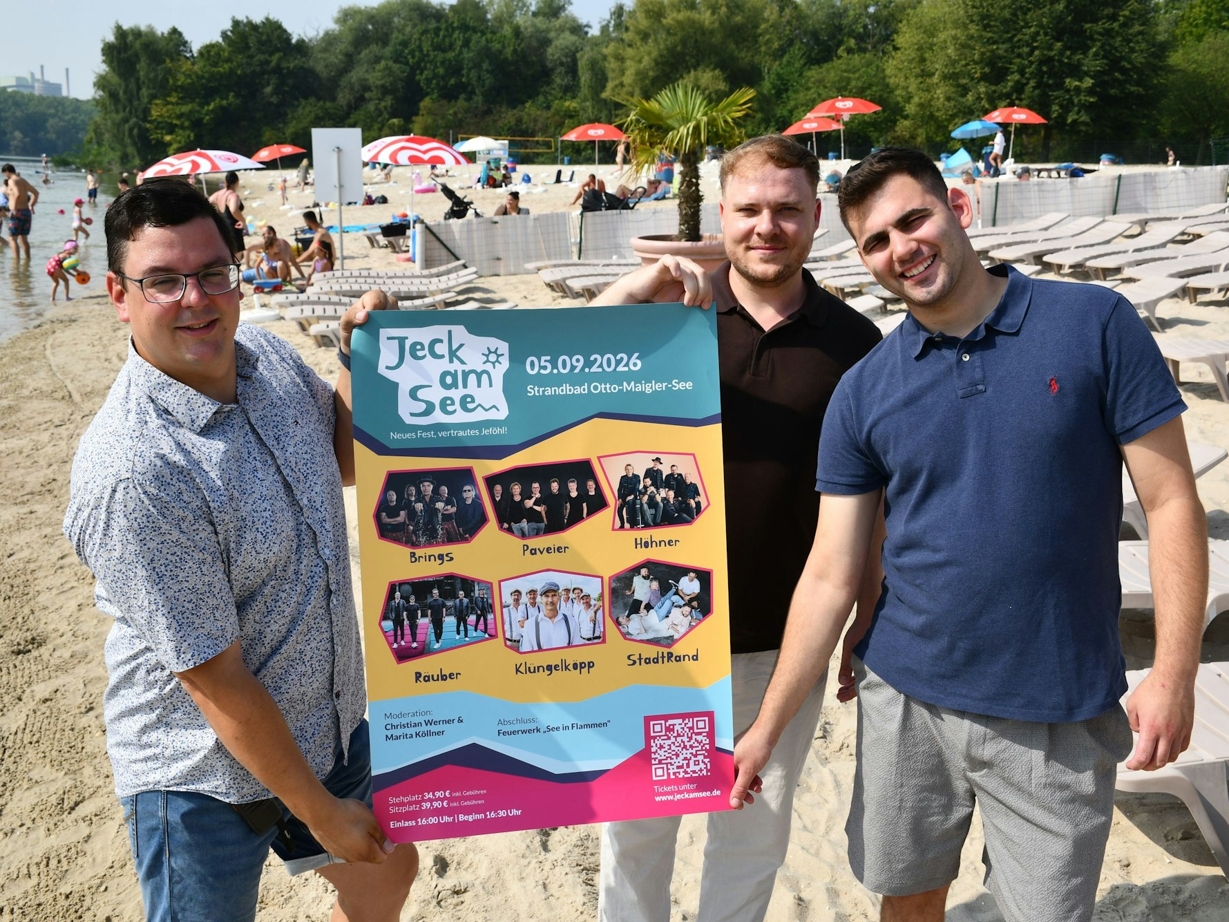 Das Foto zeigt drei Männer lockerer Kleidung im Strandbad, die ein Plakat halten.