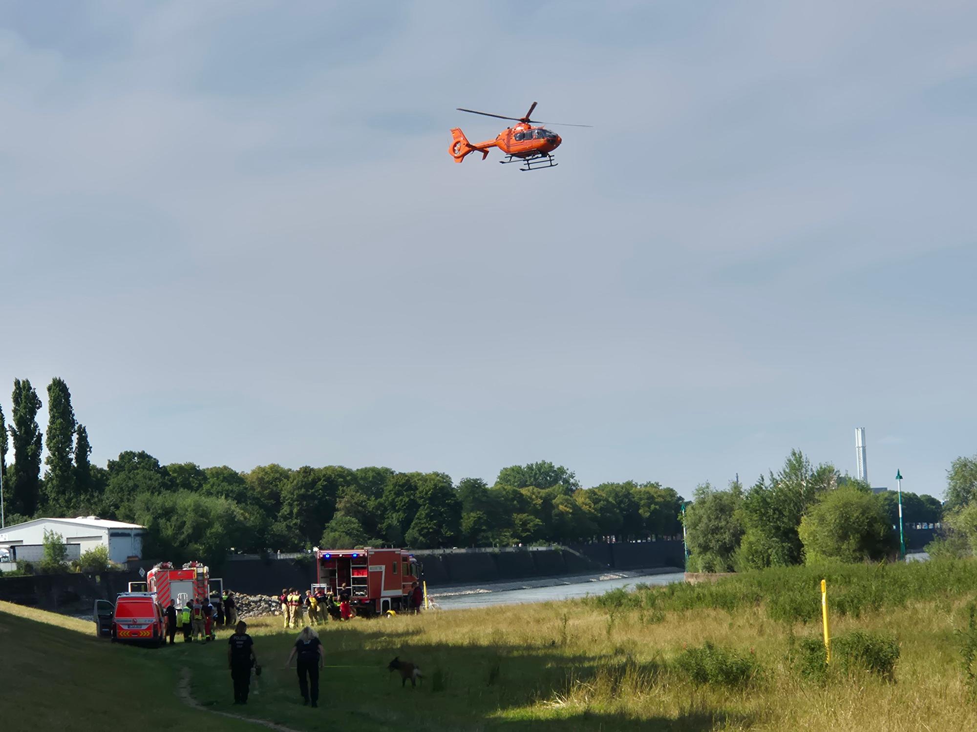 Ein Hubschrauber fliegt über einem Fluss, an dem Einsatzkräfte stehen.