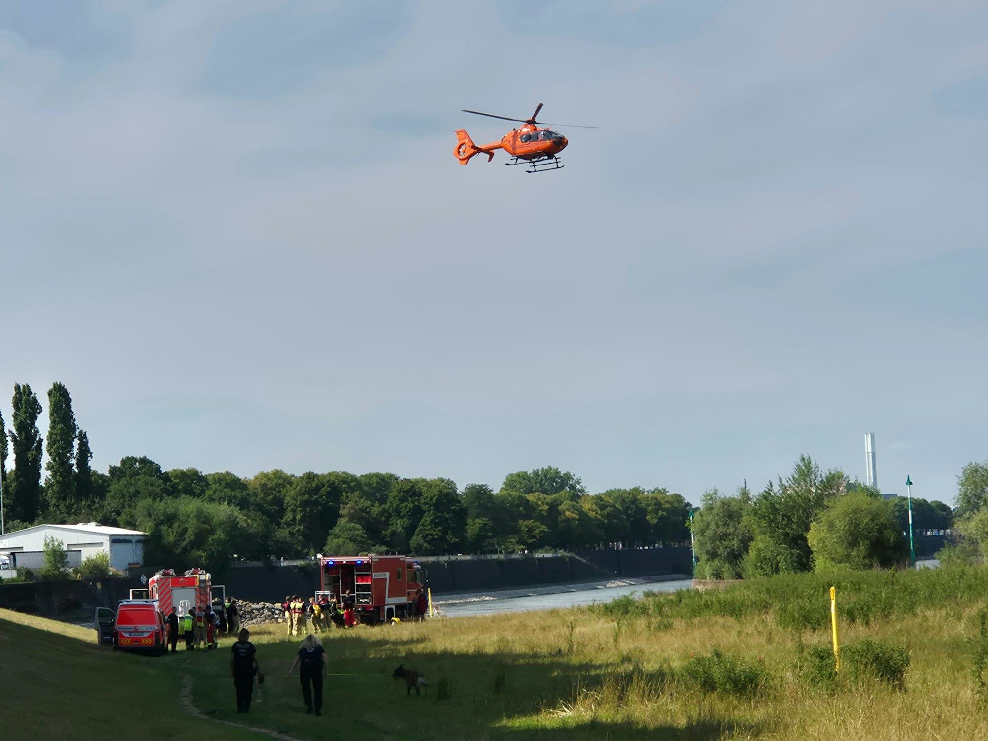 Ein Hubschrauber fliegt über einem Fluss, an dem Einsatzkräfte stehen.
