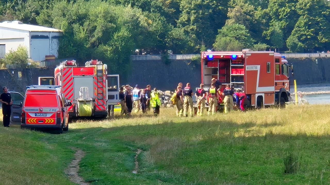 Einsatzfahrzeuge der Feuerwehr und des Rettungsdienstes sowie mehrere Einsatzkräfte stehen an einem Fluss.