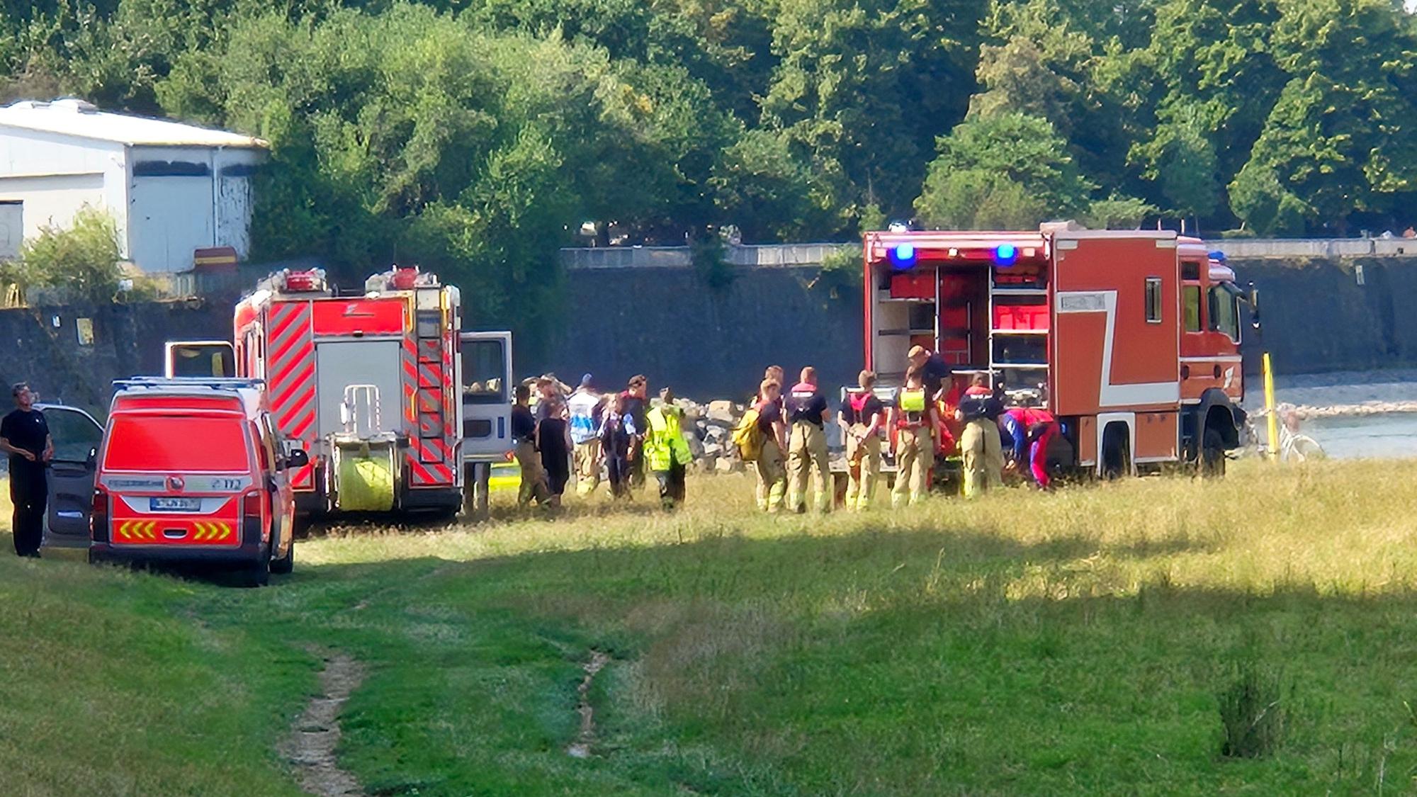 Einsatzfahrzeuge der Feuerwehr und des Rettungsdienstes sowie mehrere Einsatzkräfte stehen an einem Fluss.