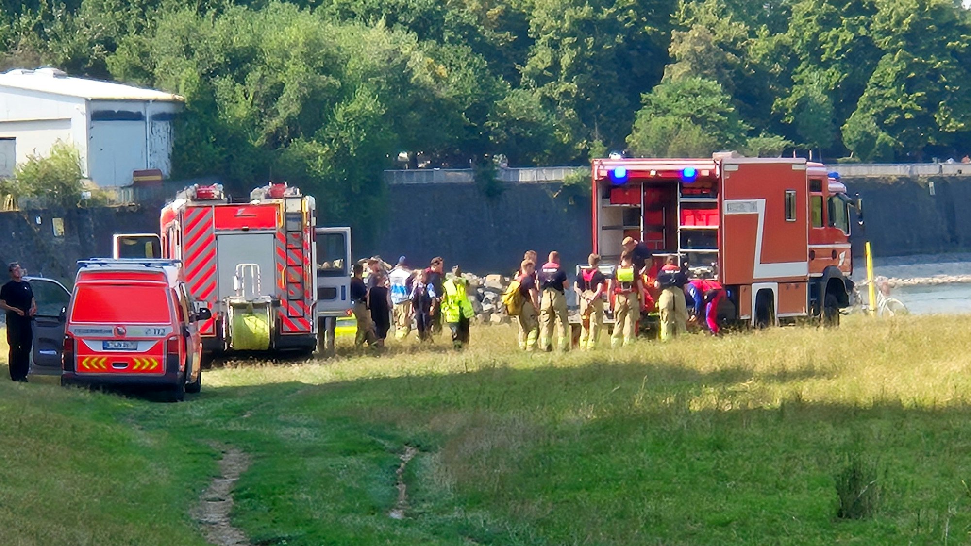 Einsatzfahrzeuge der Feuerwehr und des Rettungsdienstes sowie mehrere Einsatzkräfte stehen an einem Fluss.