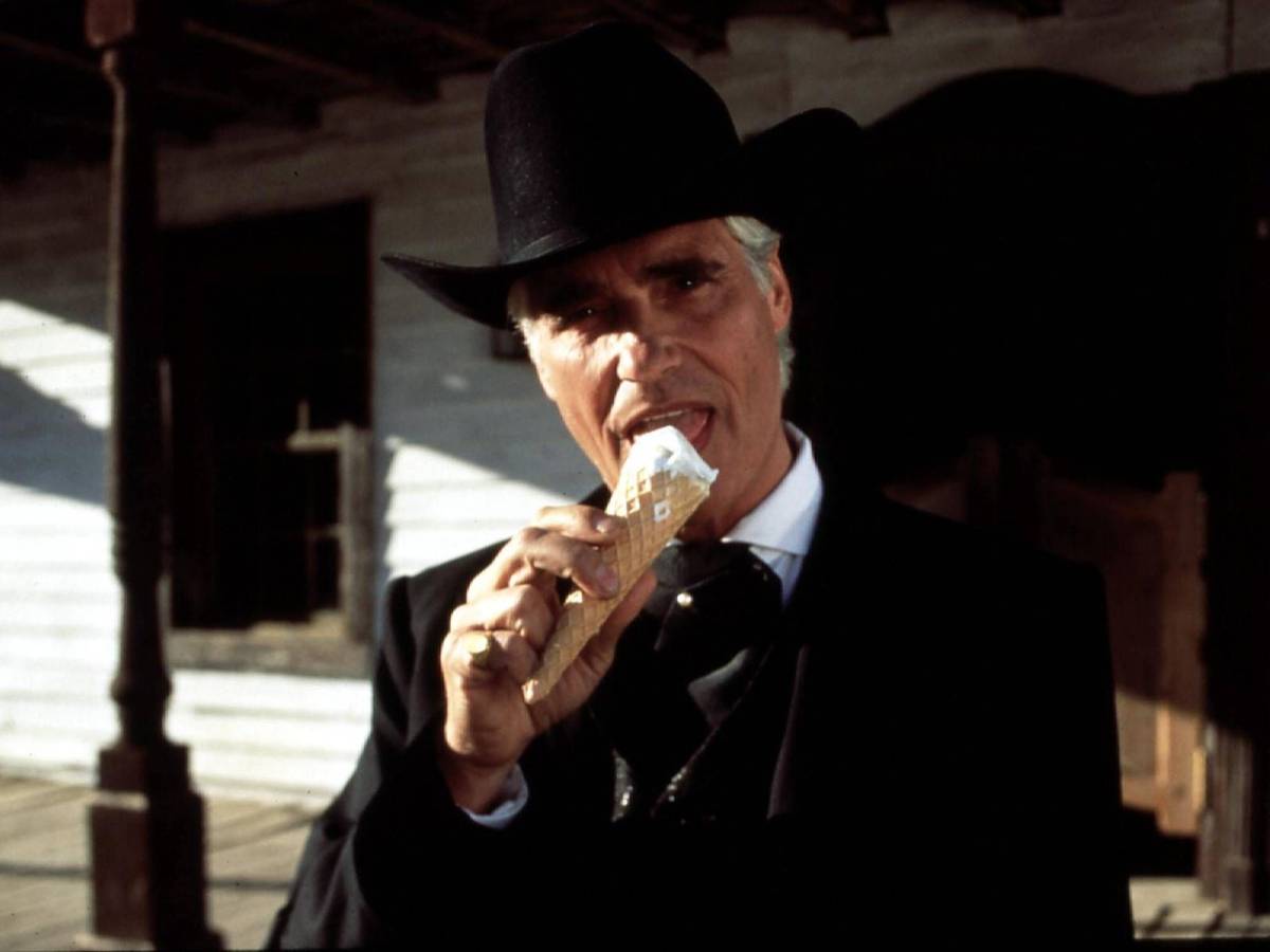 Ein Mann in schwarzer Jacke und mit schwarzem Cowboyhut leckt an einem Eis