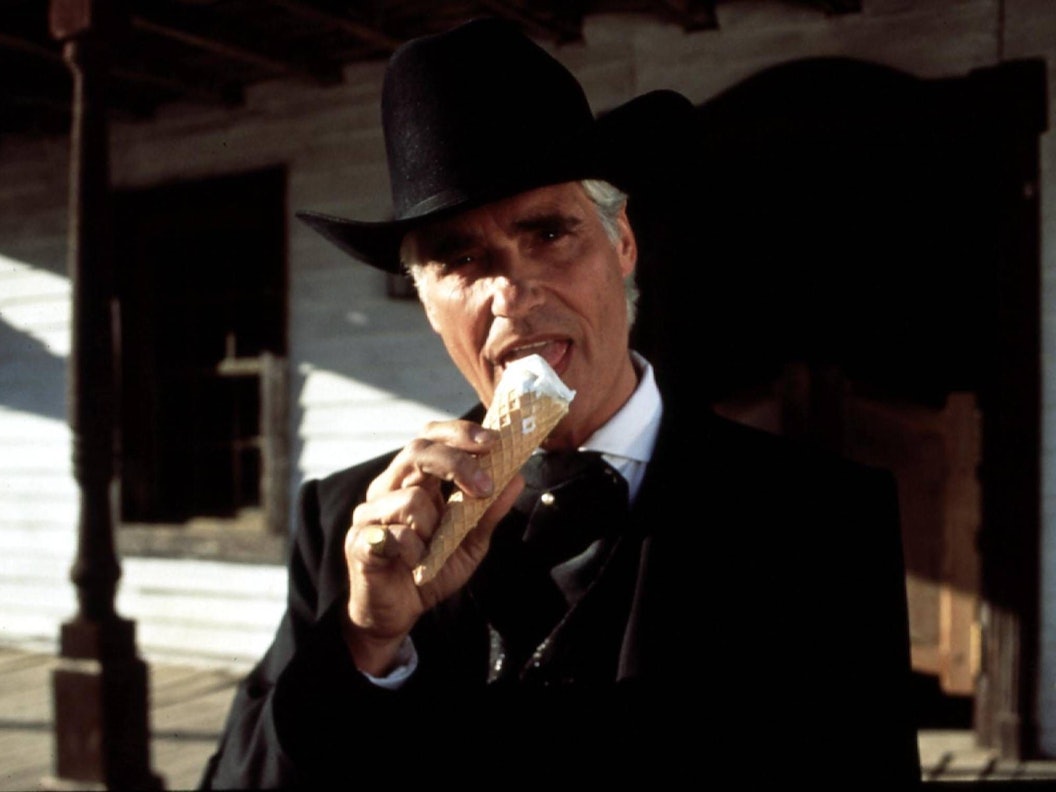 Ein Mann in schwarzer Jacke und mit schwarzem Cowboyhut leckt an einem Eis