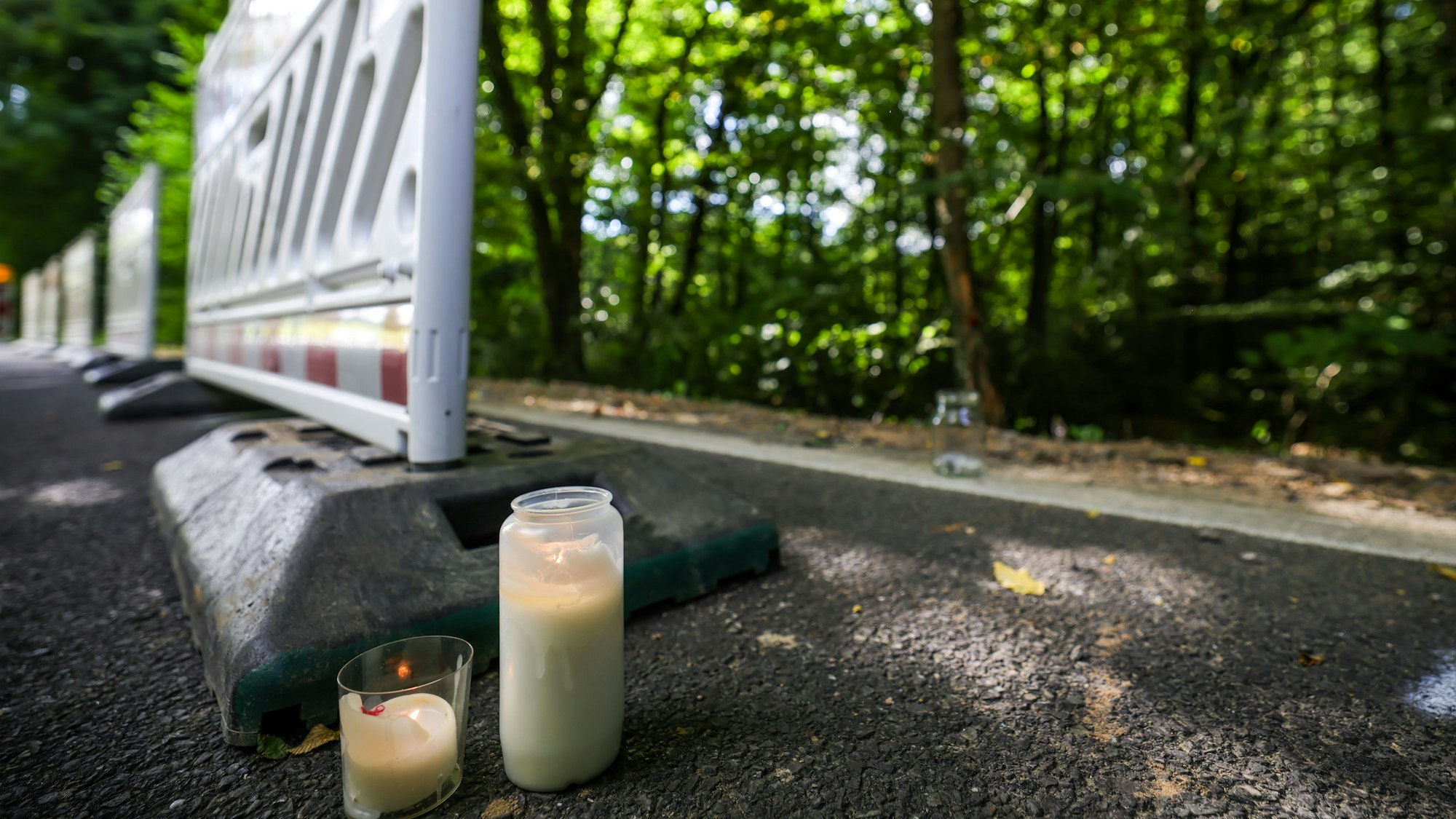 Zwei Kerzen stehen am Straßenrand in der Nähe der Unfallstelle neben Absperrgittern in Kürten