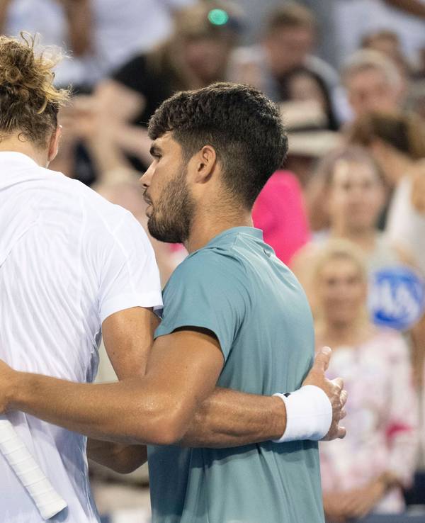 Carlos Alcaraz steht neben Alexander Zverev am Netz und nimmt ihn in den Arm.