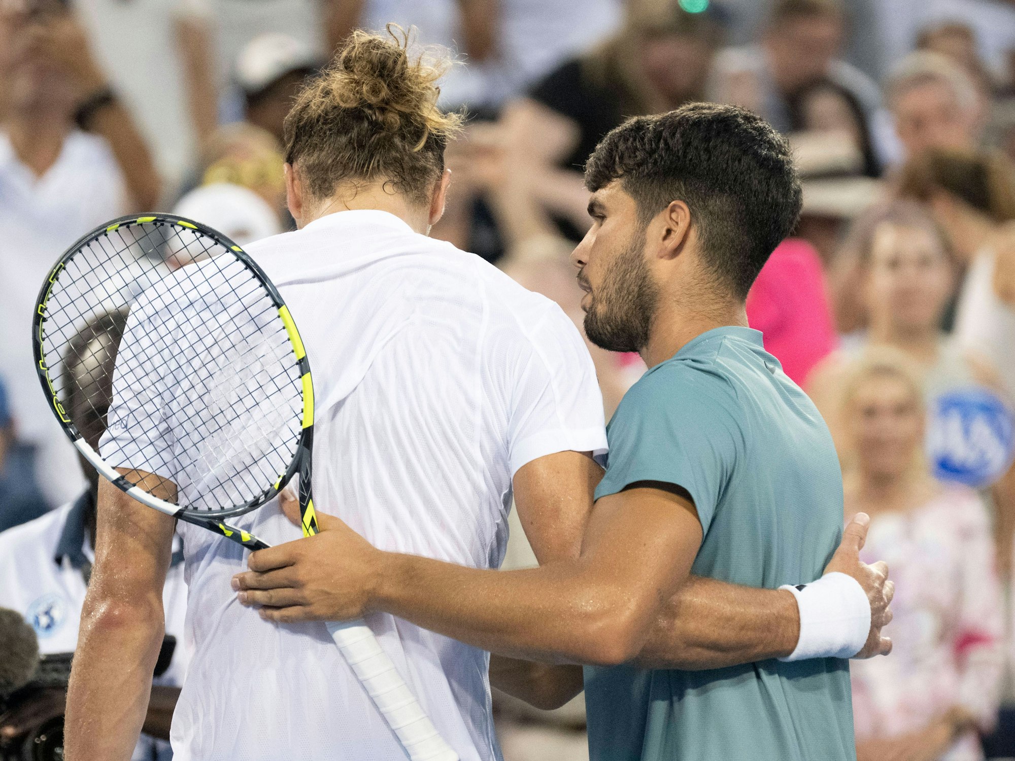 Carlos Alcaraz steht neben Alexander Zverev am Netz und nimmt ihn in den Arm.