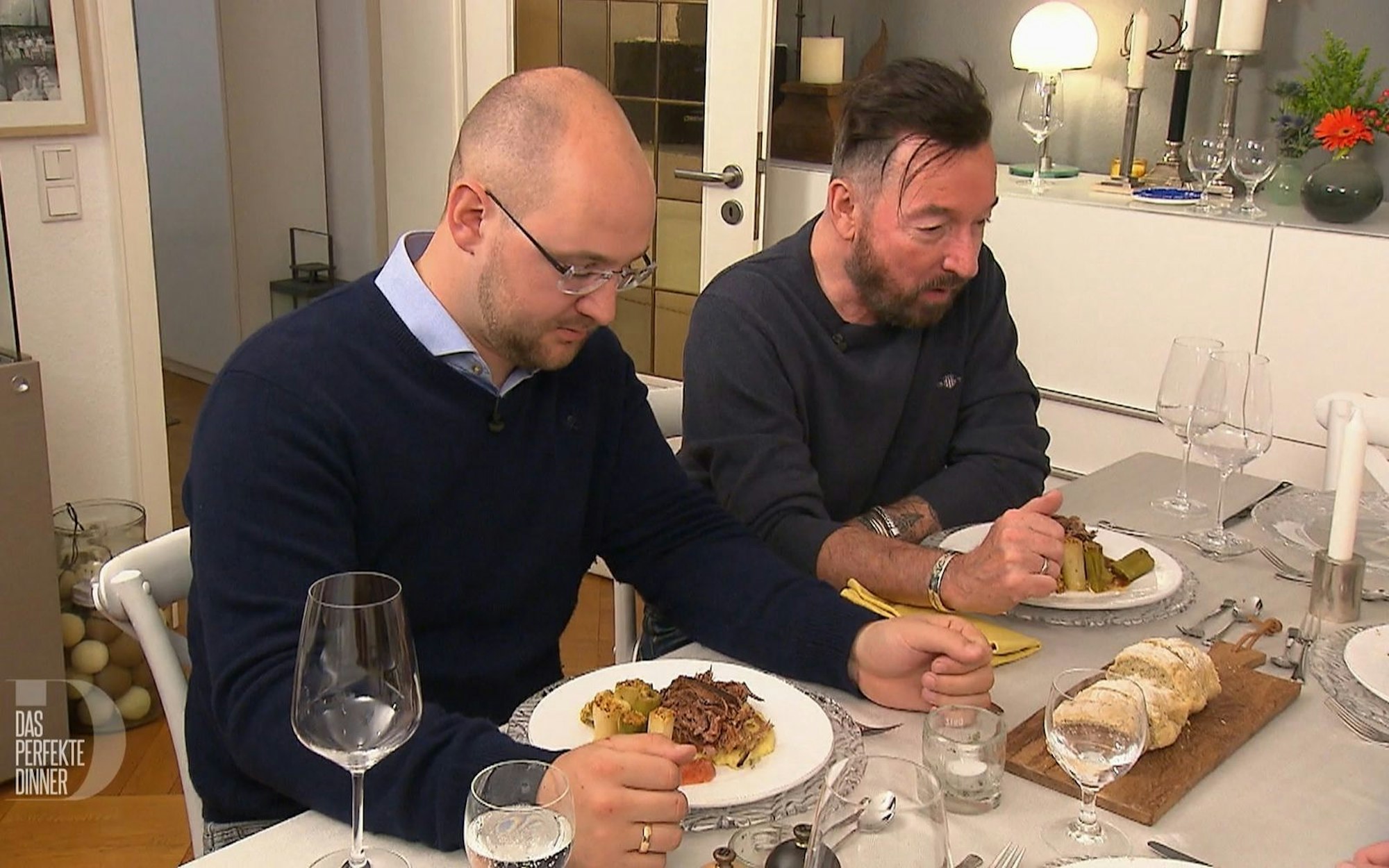 Zwei Männer sitzen nebeneinander an einem Tisch vor sich jeweils ein Teller mit der Hauptspeise.