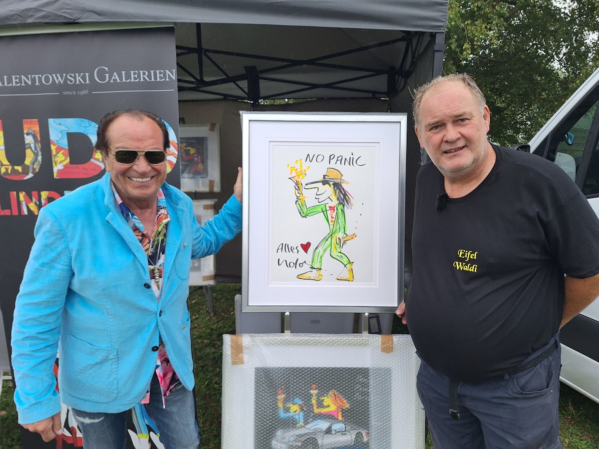 Zwei Männer halten ein Gemälde hoch, das einen tanzenden Mann mit Hut zeigt.