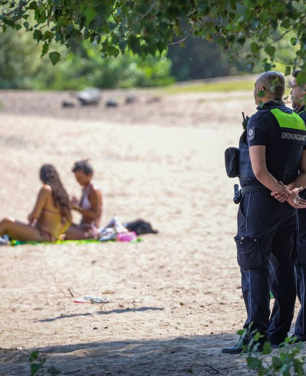 In Düsseldorf gilt das Badeverbot ebenfalls: Mitarbeiter vom Ordnungsamt der Stadt stehen an einem Strandabschnitt des Rheins und überwachen das Verbot.