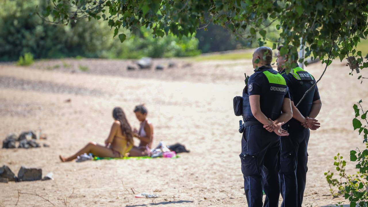 In Düsseldorf gilt das Badeverbot ebenfalls: Mitarbeiter vom Ordnungsamt der Stadt stehen an einem Strandabschnitt des Rheins und überwachen das Verbot.