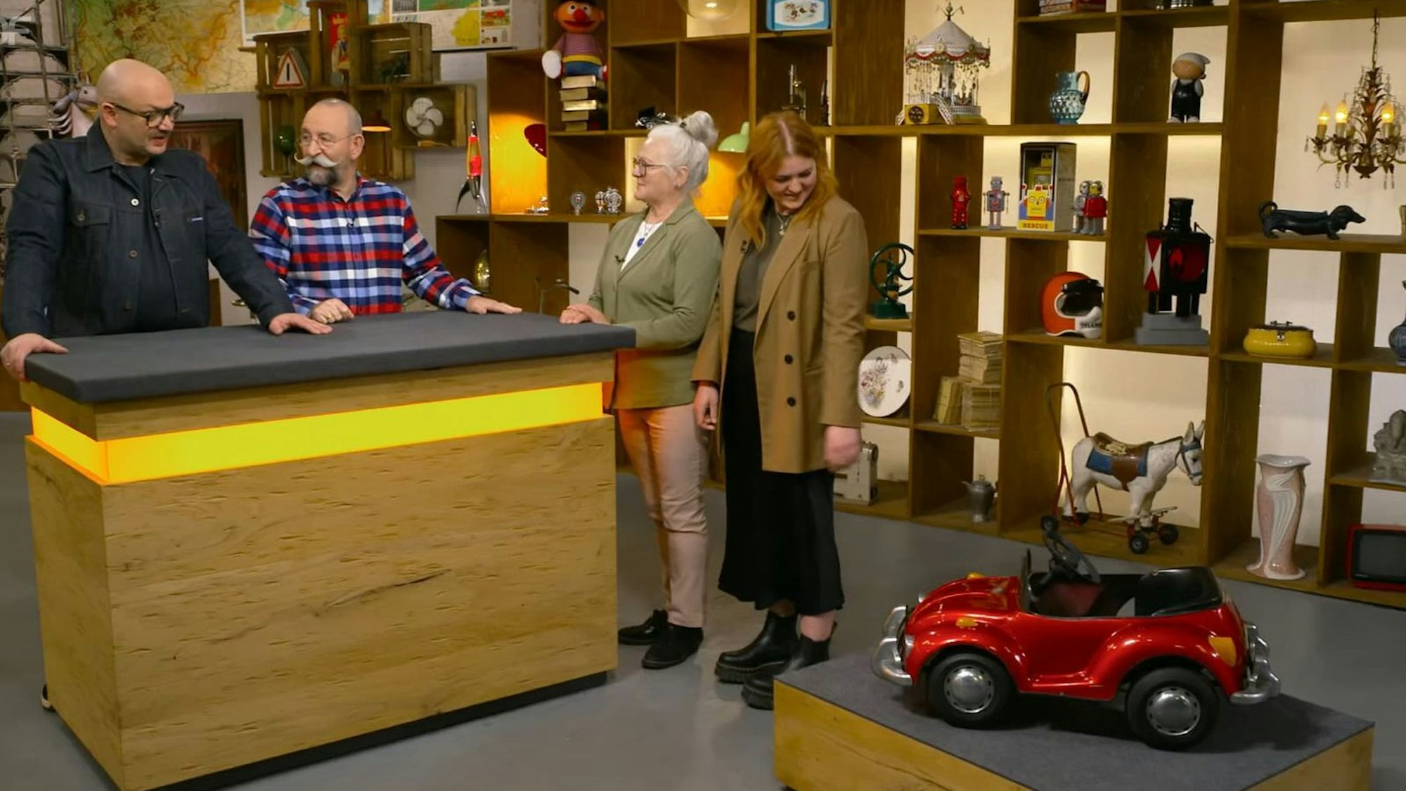 Zwei Frauen stehen neben einem Spielzeugauto und vor zwei Männern.