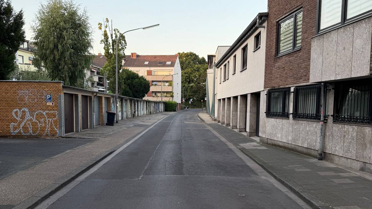 An einer Straße befinden sich Häuser und gegenüber mehrere Garagen. Kein Auto parkt hier.