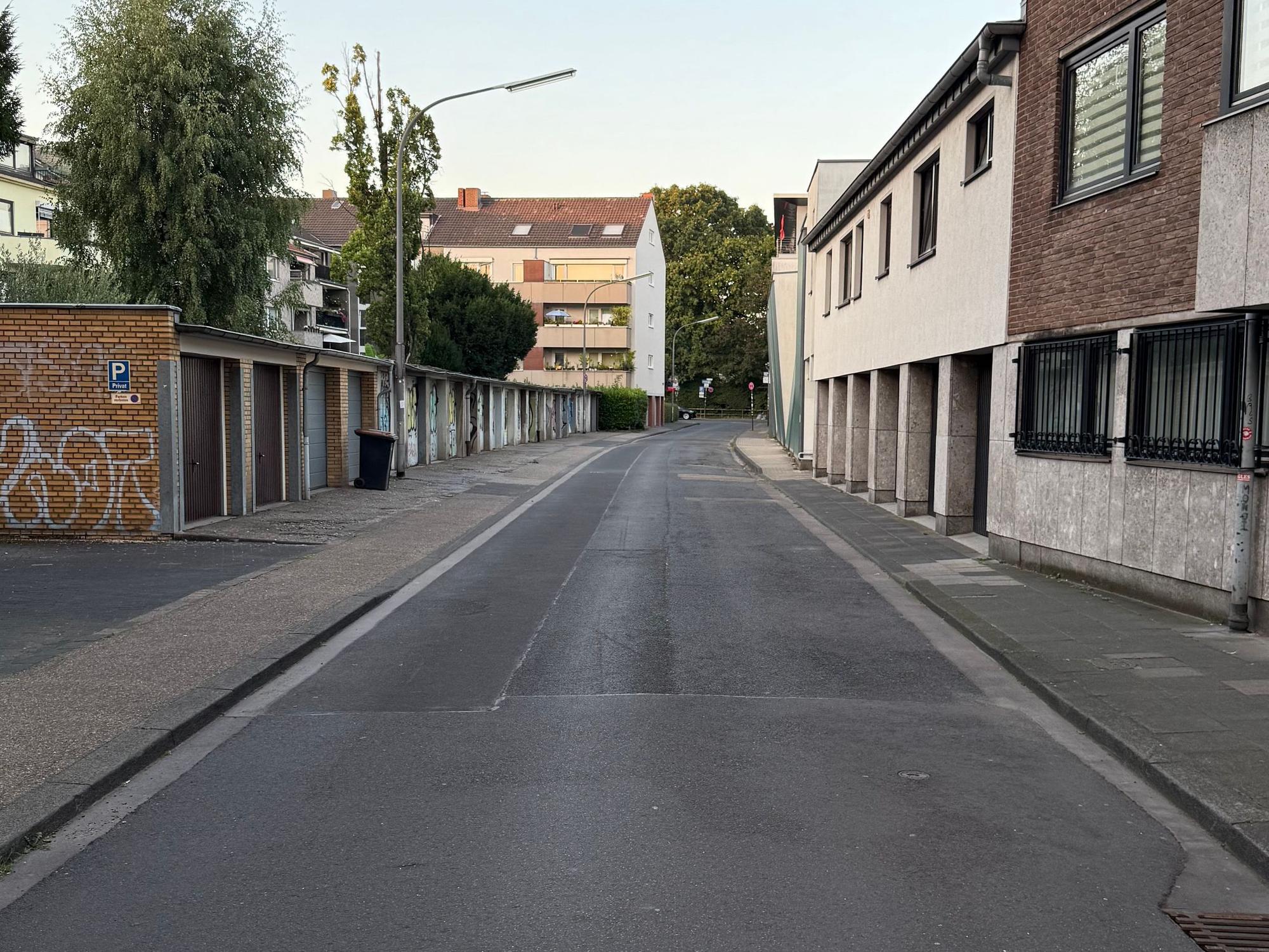 An einer Straße befinden sich Häuser und gegenüber mehrere Garagen. Kein Auto parkt hier.