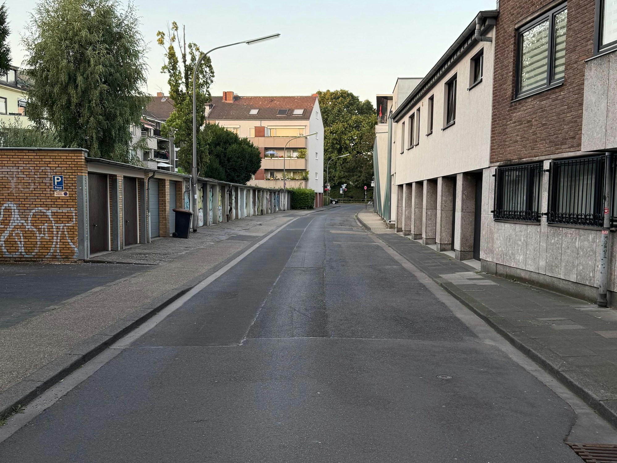 An einer Straße befinden sich Häuser und gegenüber mehrere Garagen. Kein Auto parkt hier.
