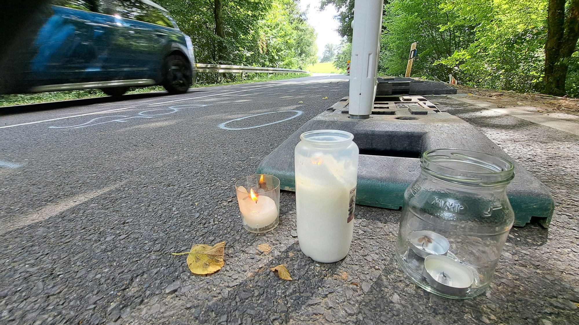Am Rande einer Straße stehen drei Kerzen.