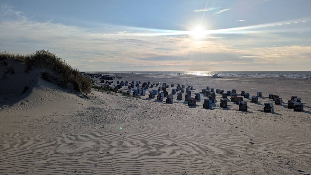Die Sonne steht tief am Horizont über einem Sandstrand mit vielen Strandkörben.