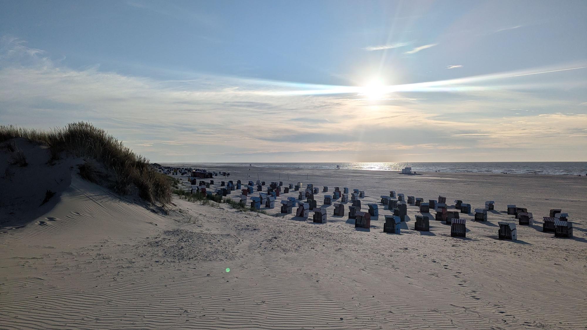 Die Sonne steht tief am Horizont über einem Sandstrand mit vielen Strandkörben.