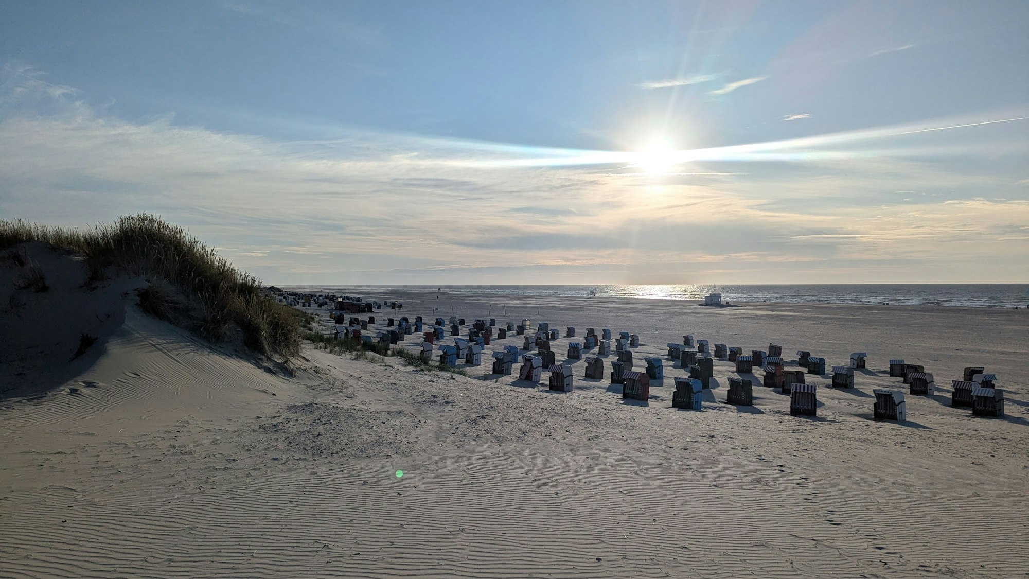 Die Sonne steht tief am Horizont über einem Sandstrand mit vielen Strandkörben.