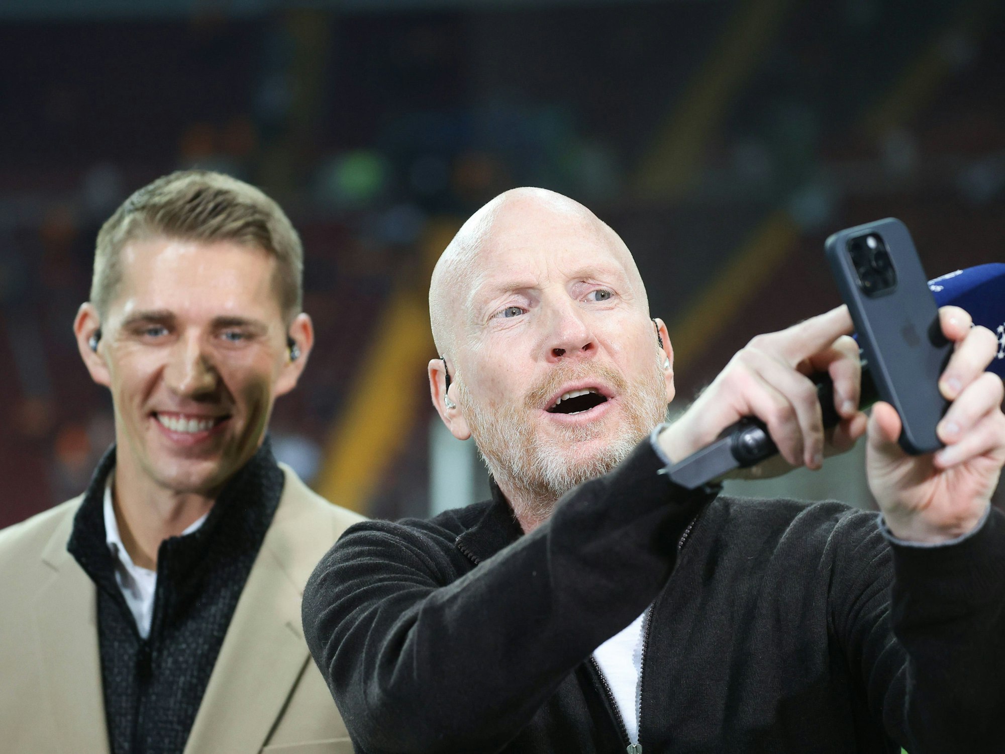 Matthias Sammer tippt auf seinem Smartphone, Nils Petersen schaut zu.