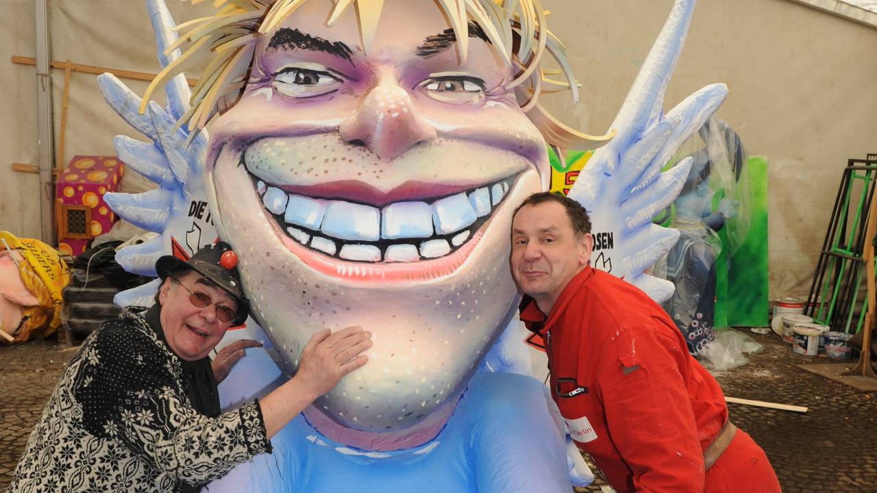 Zwei Männer lehnen sich an eine Pappfigur mit Flügeln.