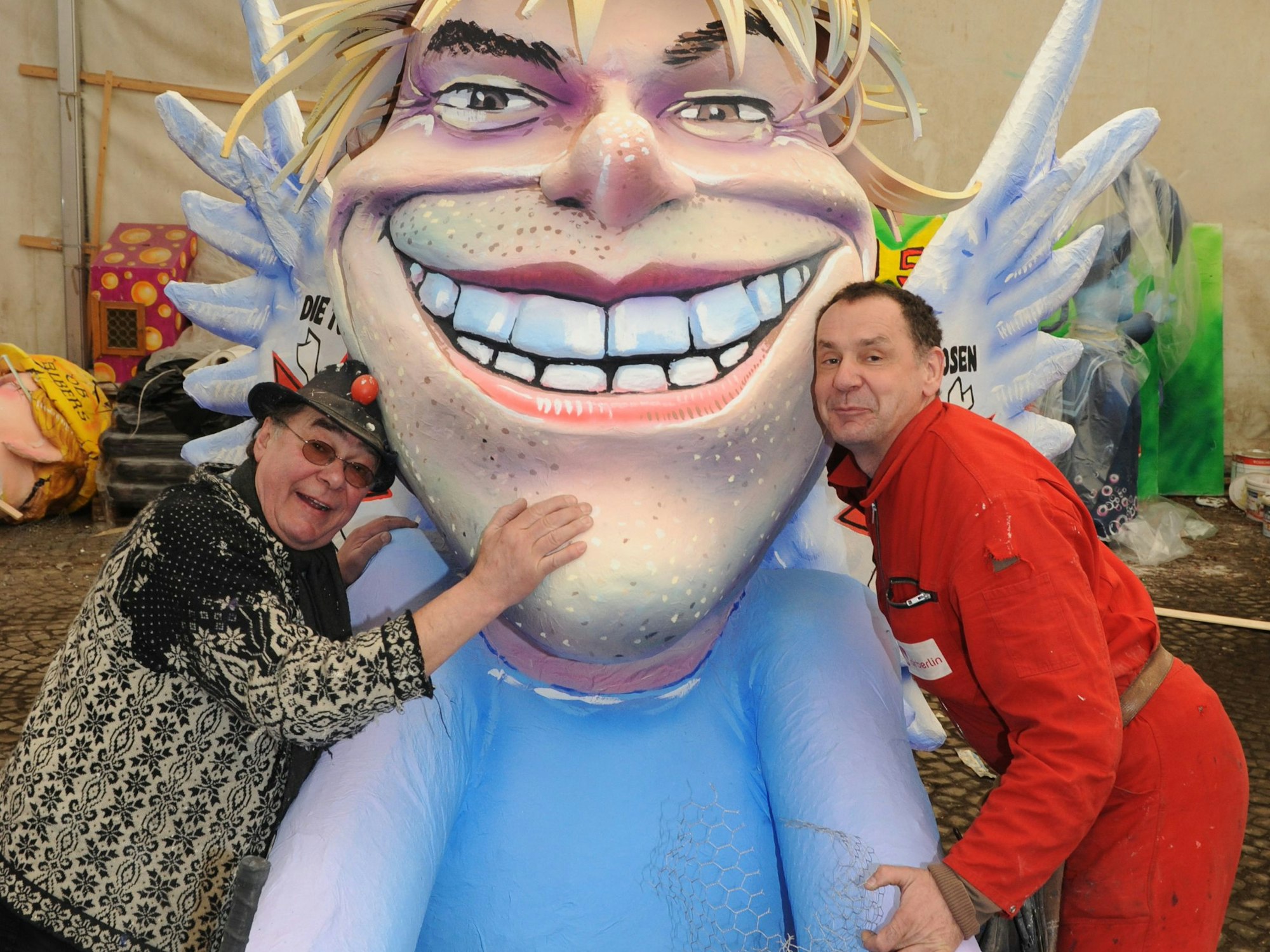 Zwei Männer lehnen sich an eine Pappfigur mit Flügeln.