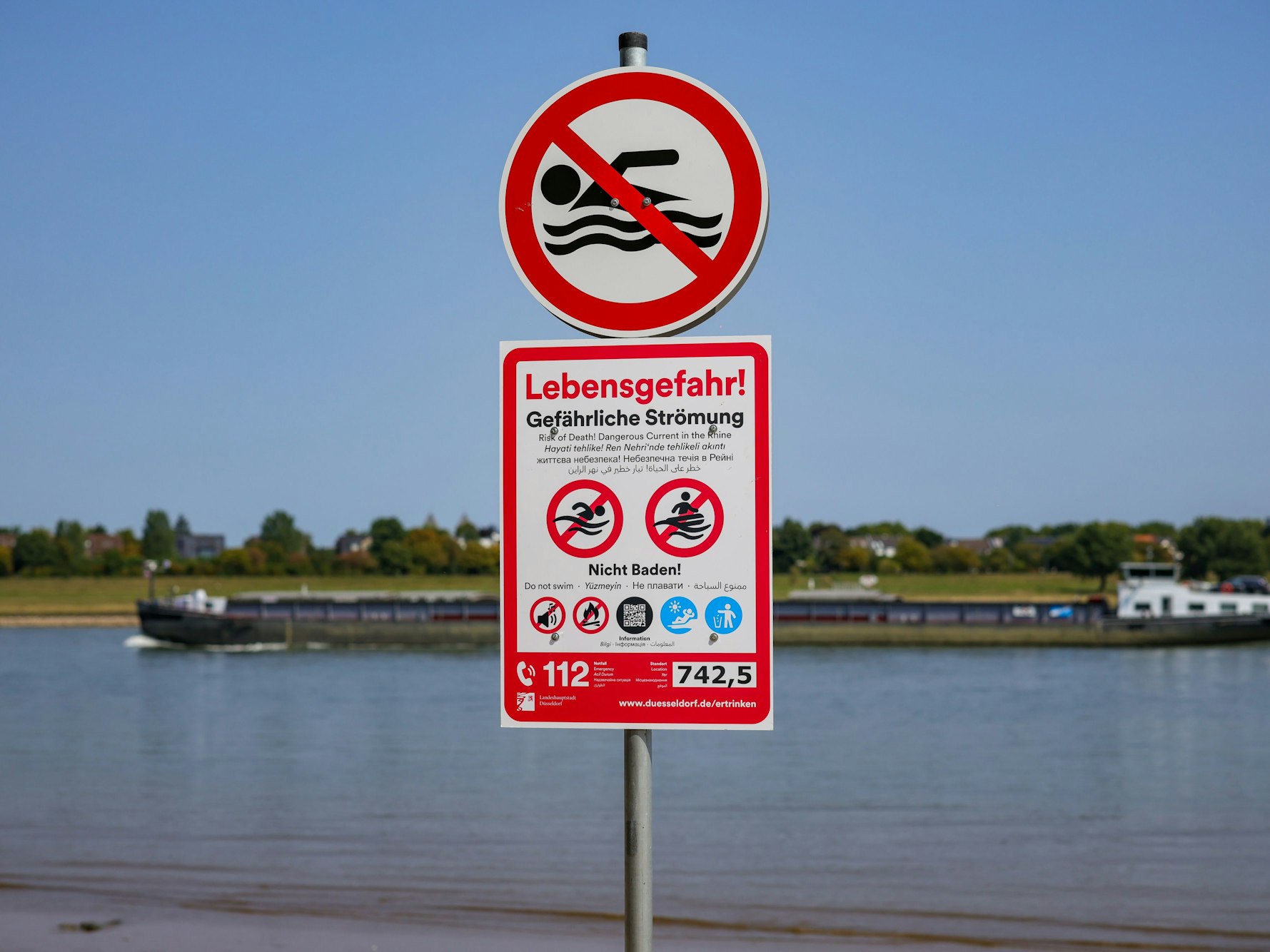 Schilder, die auf die Gefahren beim Schwimmen im Rhein und auf das ausgesprochene Badeverbot hinweisen, an einem Schildermast am Düsseldorfer Rheinufer.