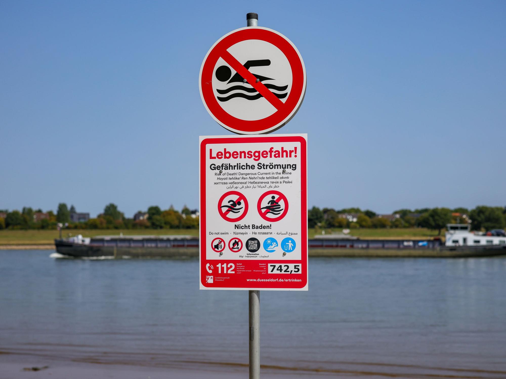 Schilder, die auf die Gefahren beim Schwimmen im Rhein und auf das ausgesprochene Badeverbot hinweisen, an einem Schildermast am Düsseldorfer Rheinufer.