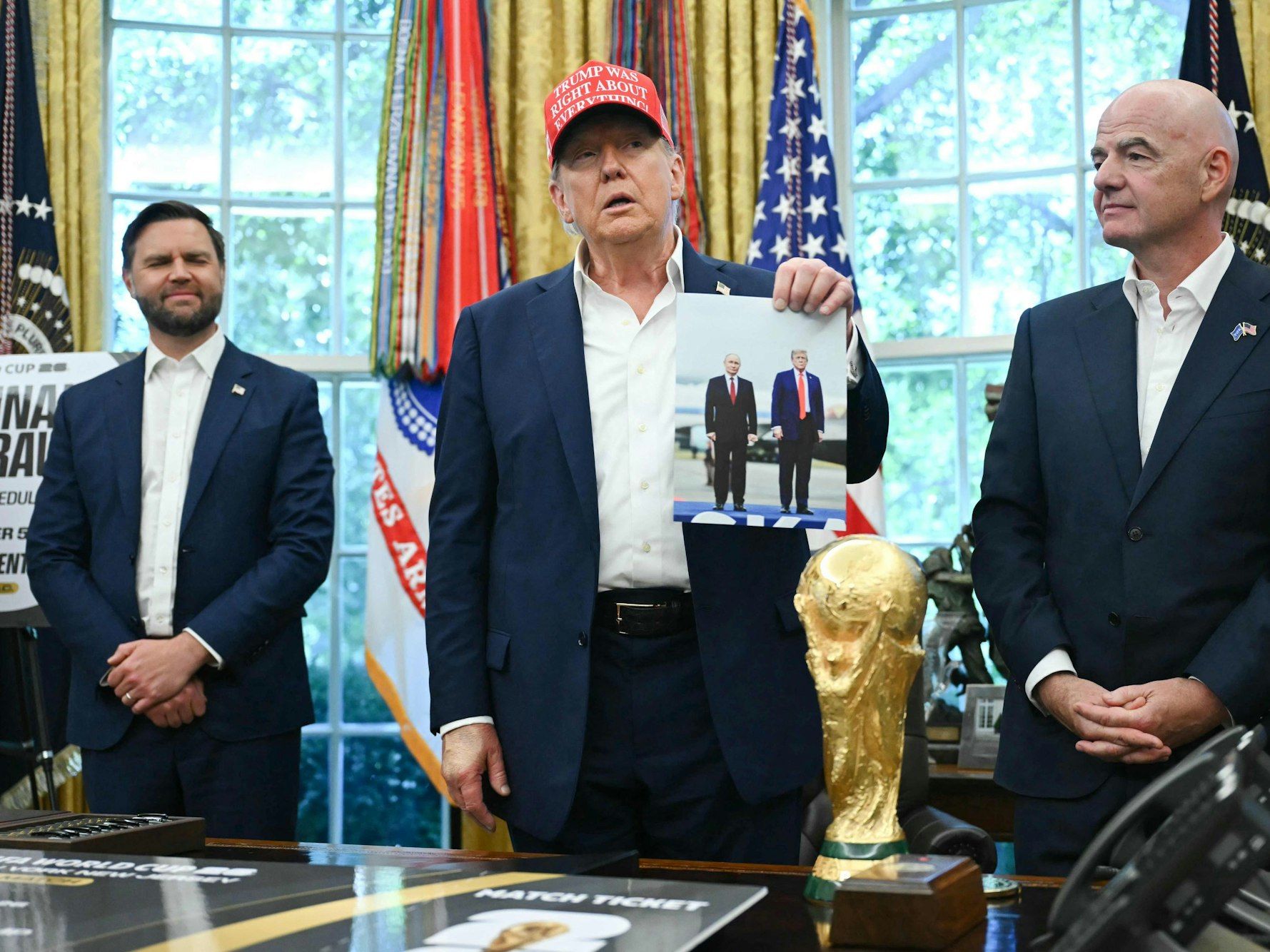US-Präsident Donald Trump (Mitte) präsentiert bei einer Pressekonferenz im Weißen Haus ein Foto von Kremlchef Wladimir Putin und ihm. Vize JD Vance und FIFA-Boss Gianni Infantino (r.) schauen zu.